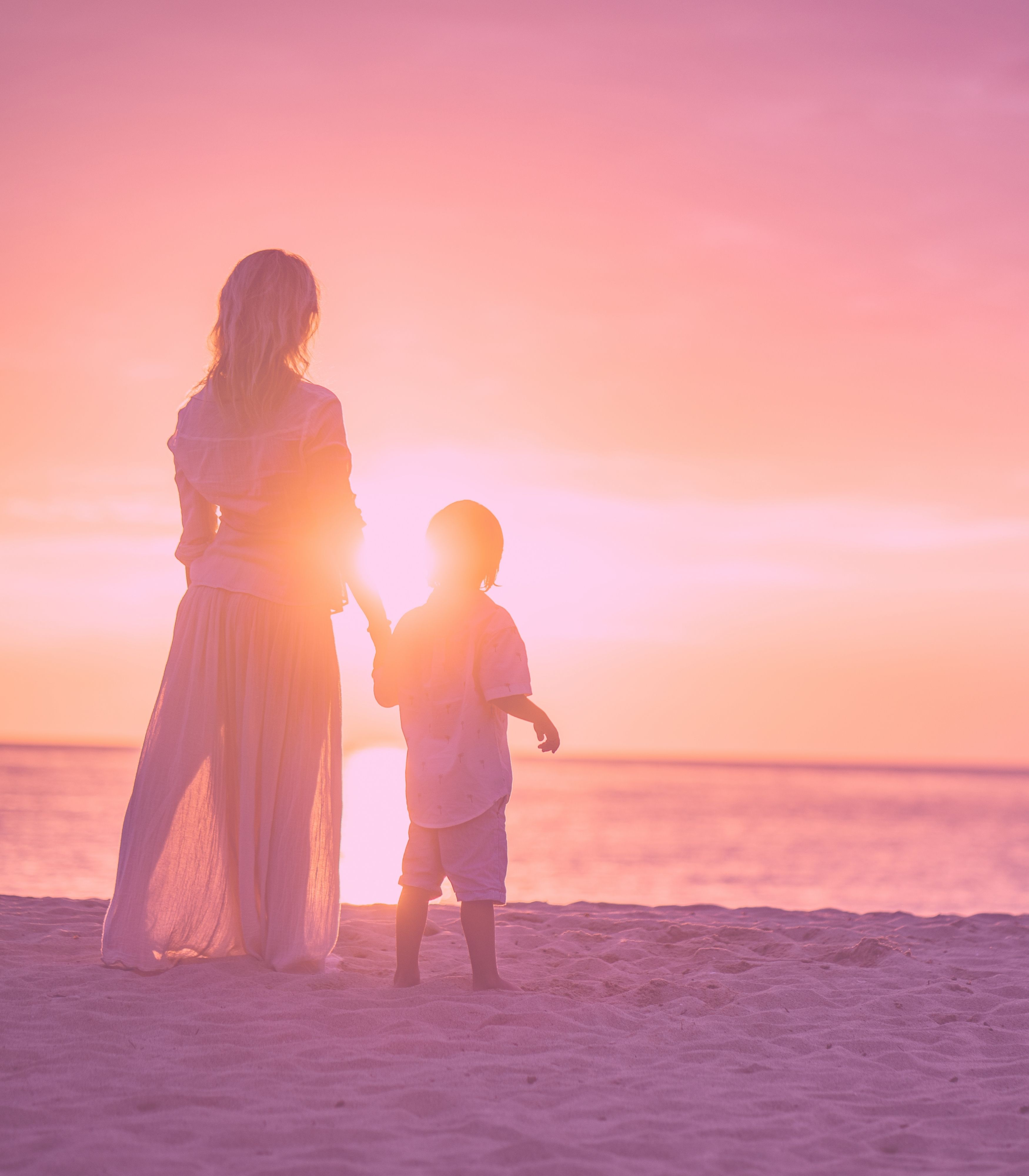 A parent and child walking together by the ocean at sunset